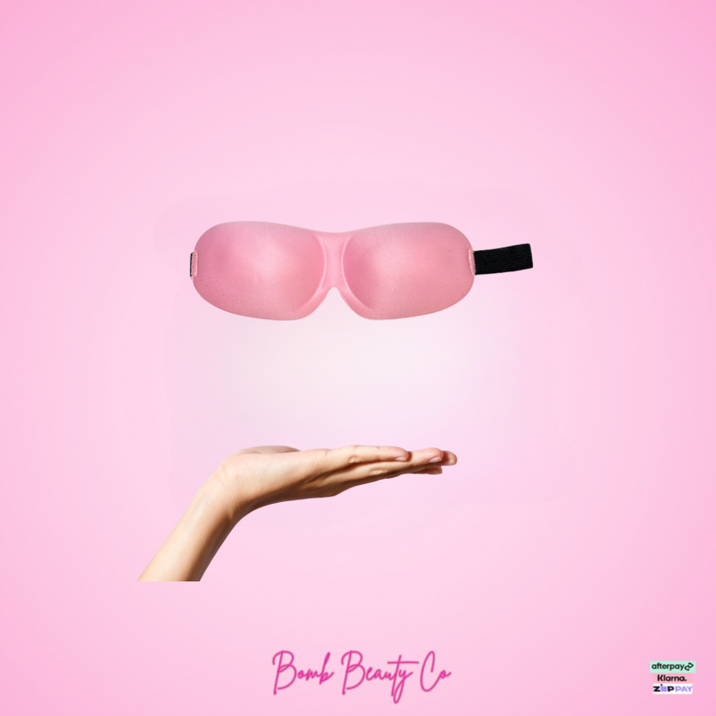 Pink sleep mask held in a hand on a pink background with 'Bomb Beauty Co' branding.