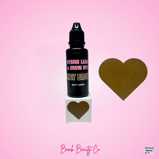 Black bottle of hybrid lash & brow dye with a gold heart on a pink background, featuring Bomb Beauty Co branding.