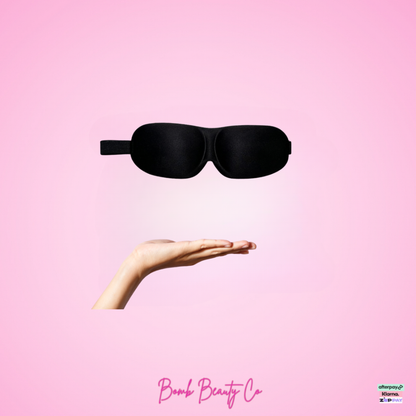 Black sleep mask held by a hand on a pink background with 'Bomb Beauty Co' branding.