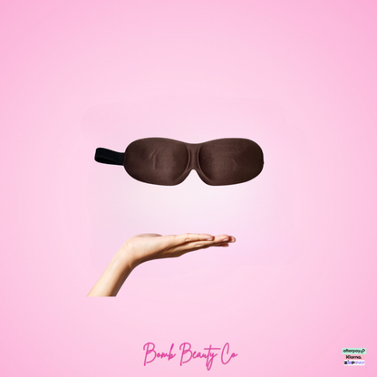 Brown sleep mask held by a hand on a pink background with 'Bomb Beauty Co' branding.