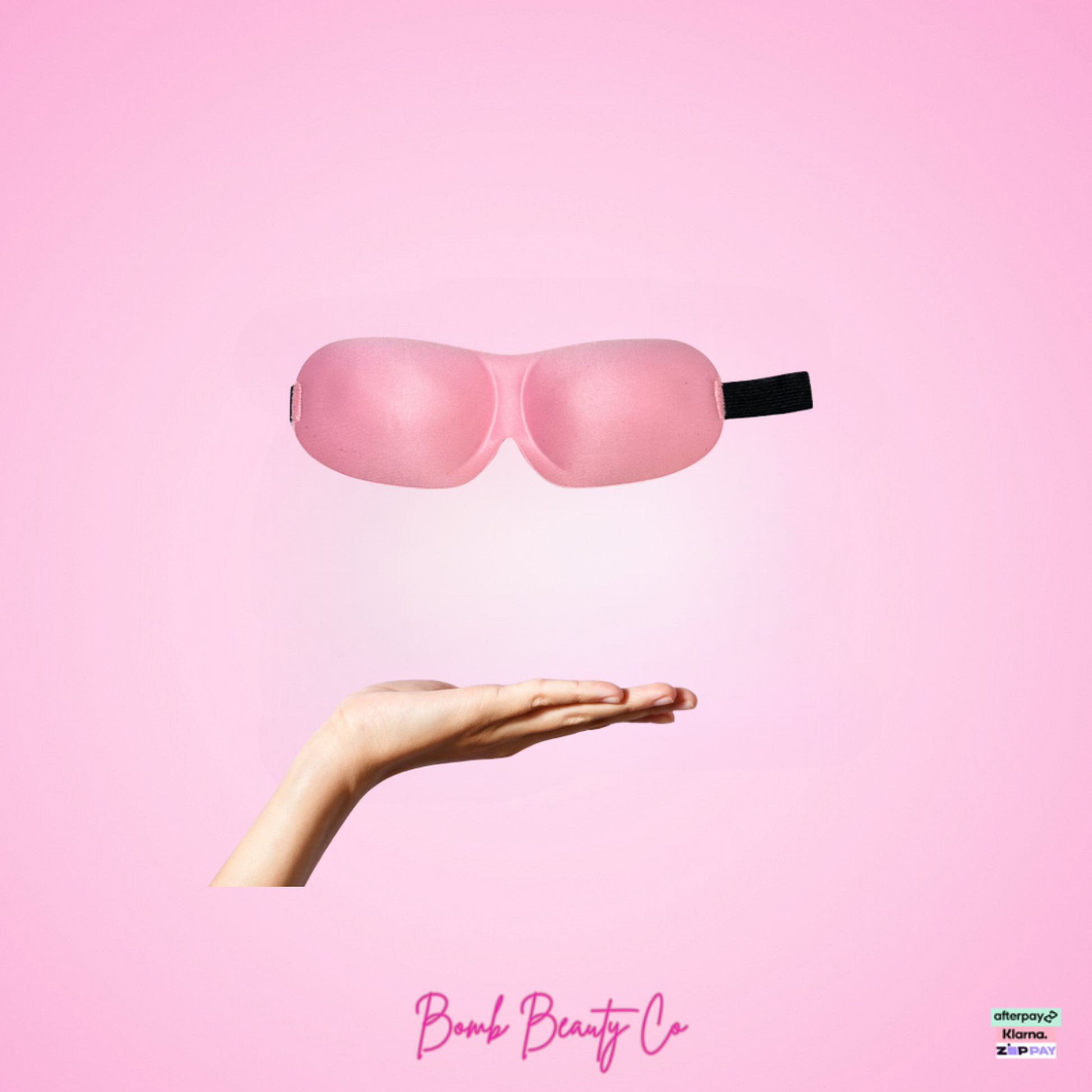 Pink sleep mask held in a hand on a pink background with 'Bomb Beauty Co' branding.